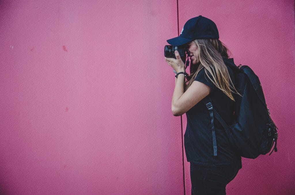 Woman standing by pink wall taking photo of online loans