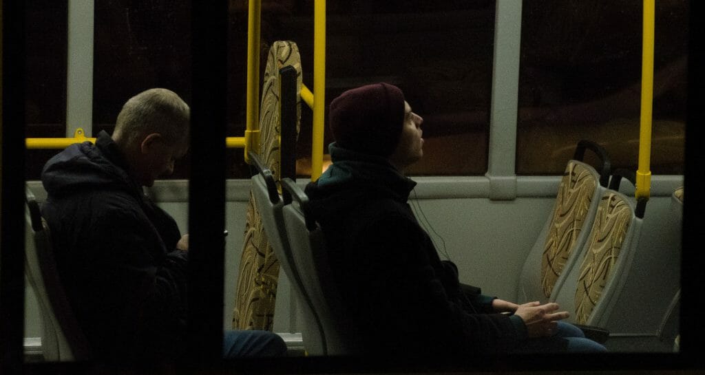 Two men sitting on bus browsing for quick loans bad credit on phone