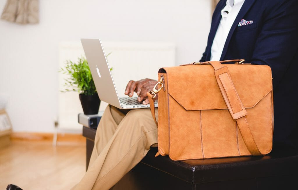 Man sitting down with brown satchel browsing for fast approval loans on laptop
