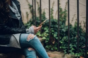 Woman wearing ripped jeans searching instant cash loans on Centrelink on her phone